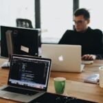 A web developer working on code in a modern office setting with multiple devices.